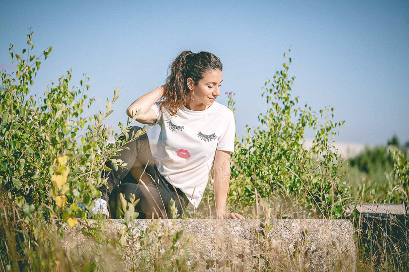 A model sits on a concrete block among green plants and looks down at the ground