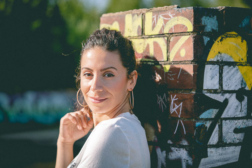 A model leans against a graffitied post and looks at the camera