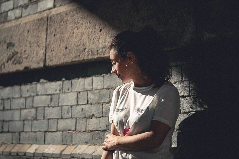 A model stands half in shadow, half in light, looking down over her right shoulder and away from the camera