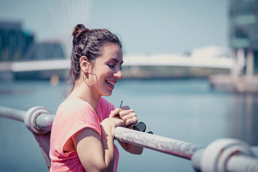 A model leans on a railing overlooking some quays and laughs