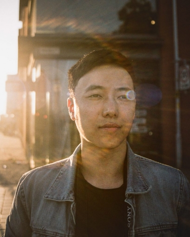 A Chinese man looks past the camera to the distance, with a sunburst across his face.