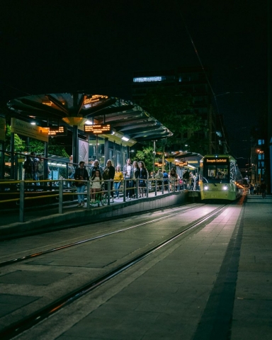 A yellow tram pulls up to a platform where people wait to board